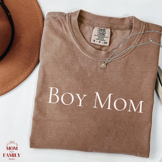 folded brown comfort colors® shirt with clean white serif text reading "Boy Mom", styled with necklace and hat for a minimalist mom aesthetic