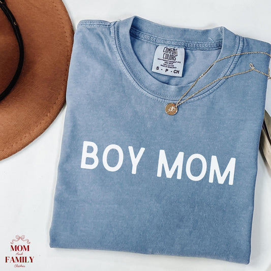 folded brown comfort colors® shirt with clean white serif text reading "Boy Mom", styled with necklace and hat for a minimalist mom aesthetic