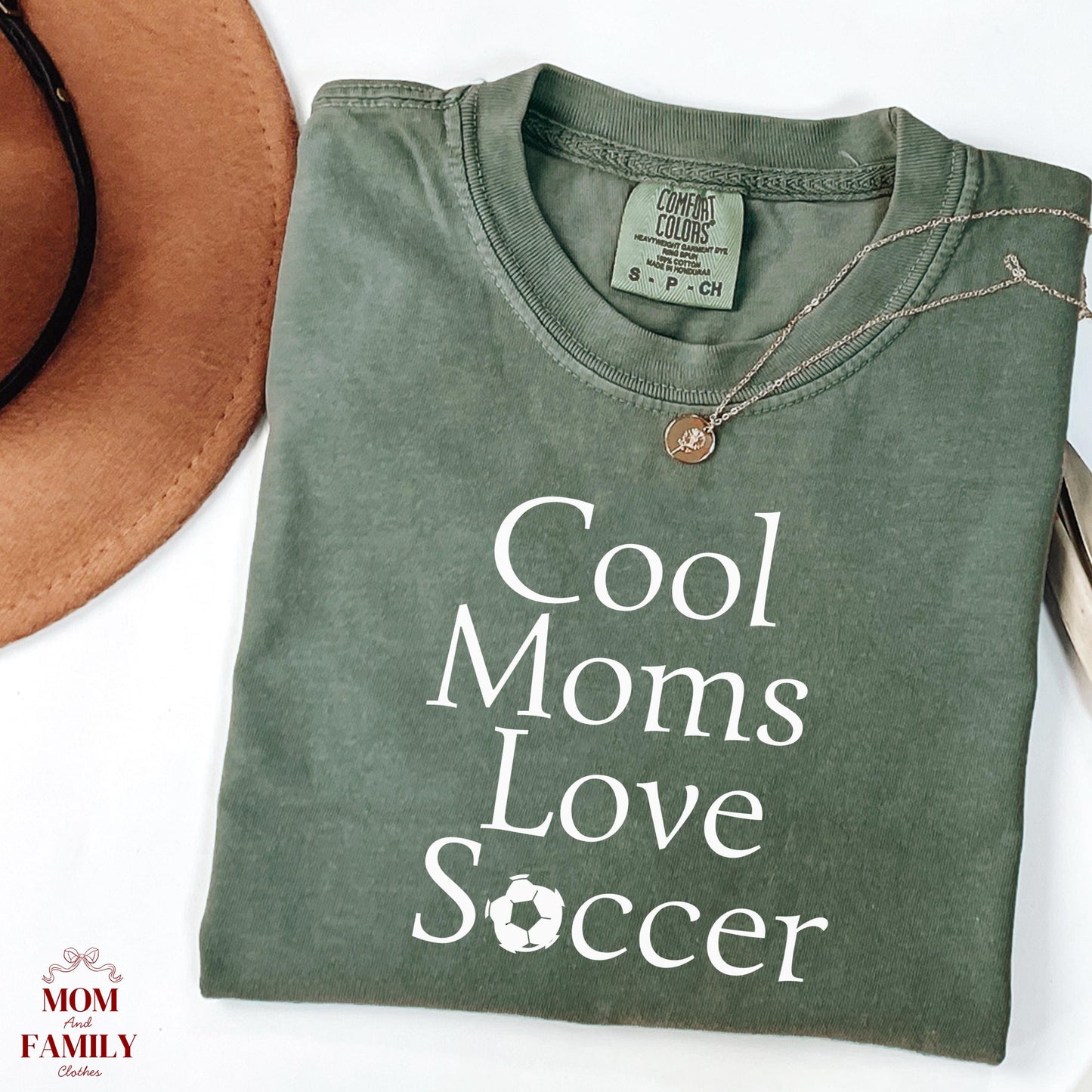 folded green comfort colors® shirt with white text "Cool Moms Love Soccer" and a soccer ball replacing the letter O, ideal for sporty moms