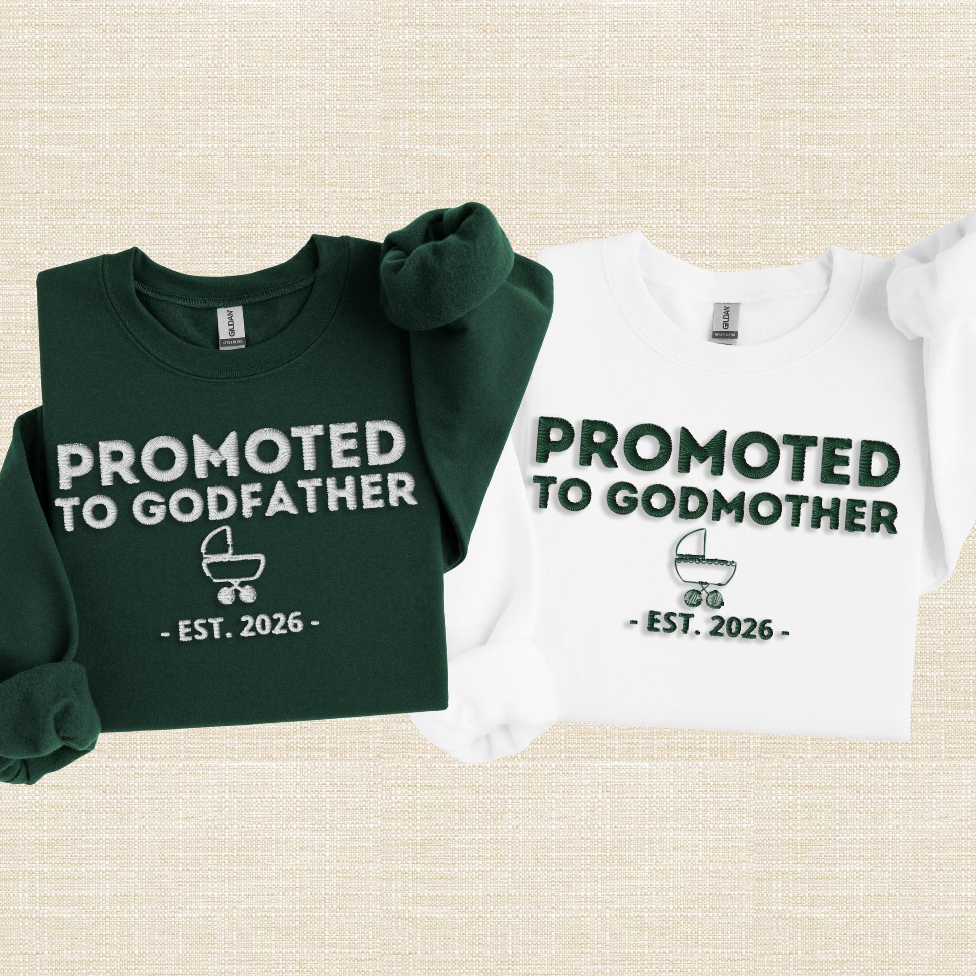 Embroidered style sweatshirt with bold “Promoted To Godmother” text, small baby carriage icon, and “EST. 2026” below, shown in white crewneck with raised stitch look.